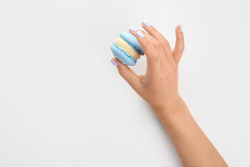 Woman with neat manicure holding delicious macaron on white background