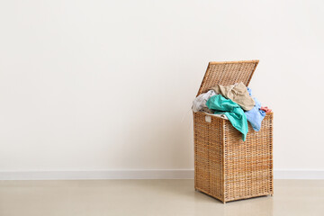 Wicker basket full of dirty clothes near light wall