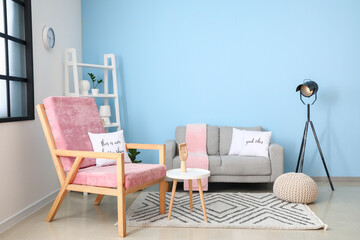 Interior of stylish room with comfortable armchair and sofa near color wall