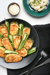 Plate with tasty jalapeno poppers and sauce on white background