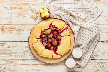 Board with tasty plum galette, butter, sugar and flour on light wooden background