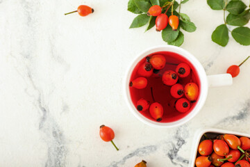 Cup of tasty rose hip tea and berries on white marble background