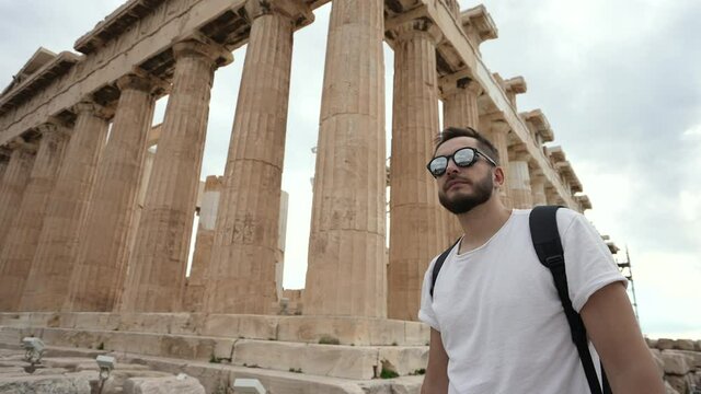 Tourist among pillars of ancient temple, walking and looking around, mesmerized by Greek architecture. Traveler on sight of Acropolis in Athens. Tourism, traveling to ruins of ancient civilization.