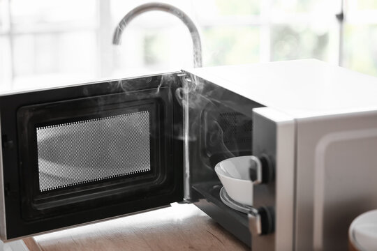 Damaged Microwave Oven With Smoke On Table In Kitchen, Closeup