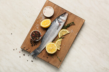 Wooden board with fresh uncooked sea bass fish, lemon and spices on white marble background