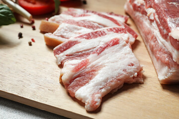 Wooden board with slices of uncooked bacon on table