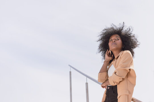 Elegant Young Black Woman With Afro Looking Straight Ahead Leaning Against A Handrail With Copy Space To The Left