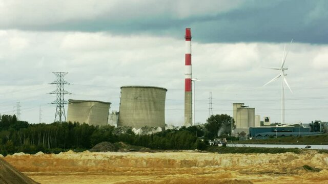 Two cooling towers imploding with controlled demolition on a cloudy day