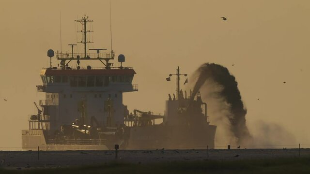 Dredging Vessel At Work In Open Sea With Birds Flying At Sunset. wide, slow motion