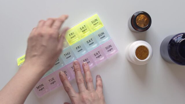 Female hands open pillbox with weekly vitamins and nutrients. Bottles with pills on background on white table. Healthcare and medicine concept