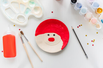 The child glues the parts Santa made from paper plate. Handmade. Project of children's creativity, handicrafts, crafts for kids. Preparation for christmas. Decoration.