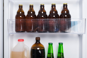 against the background of a white refrigerator door, glass bottles with beer and drinks are on the shelf