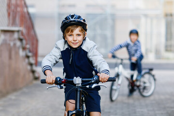 Two school kid boys in safety helmet riding with bike in the city with backpacks. Happy children in...