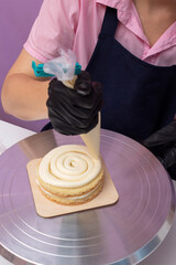 Laying out cream from pastry bag, which is held by gloved hand. Process of creating bento cake. Selective focus.
