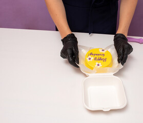Woman puts yellow bento cake in box container. Packaging for delivery. Selective focus.