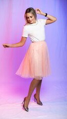 beautiful woman portrait in studio posing. A girl in a white blouse, a T-shirt and a pink, peach pleated skirt laughs, spins, dances. colored, crimson purple background. holiday, new year, birthday