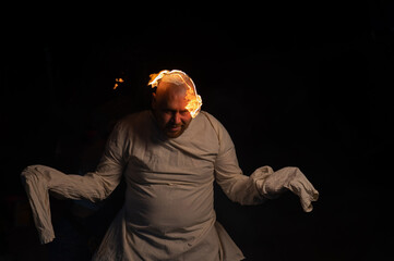 Bald man in a straitjacket with a burning head on a dark background.