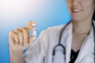 A doctor in white coat and stethoscope around her neck is holding a glass bottle of BCG vaccine...