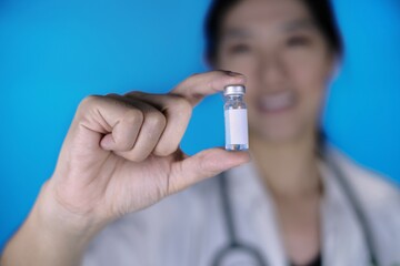 A attractive doctor, wearing a white coat with a stethoscope around her shoulder, holding a glass vial of vaccine bottle with blank white label, smiling. Healthcare And Medical concept.