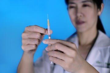 A female Asian doctor holding up a syringe with covid-19 vaccine, measuring the dosage before...