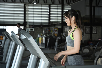 Fototapeta na wymiar Young woman in sportswear running on treadmill in a gym.