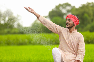Fototapeta premium Indian farmer spreading fertilizer in the green agriculture field.