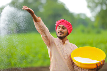 Indian farmer spreading fertilizer in the green agriculture field.