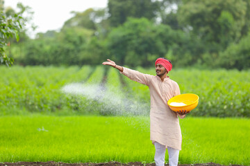 Indian farmer spreading fertilizer in the green agriculture field.