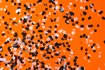 White black confetti flying on orange background. Halloween party.