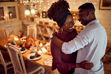 Embraced black couple has fun while celebrating Thanksgiving in dining room at home.