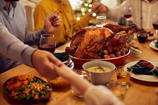 Close-up Of Family Saying Grace While Holding Hands During Thanksgiving Meal At Dining Table.