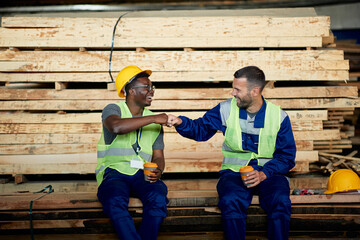 Happy warehouse workers greet with fists on coffee break at wood compartment.