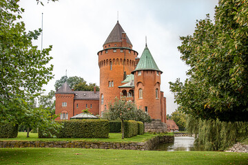 Fototapeta na wymiar Hjularod is a romantic red castle with tall towers situated in a green park