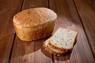 A loaf of delicious white bread made from natural products, on hops with flax saturation, without baker's yeast, on a wooden table surface.