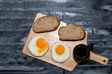 Breakfast food fried egg bread slice has espresso coffee in cutting board.