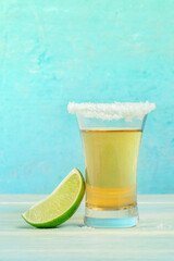 Tequila gold shot with a lime, Mexican liquor on a vibrant blue background, with a salt rim, side view with a place for text