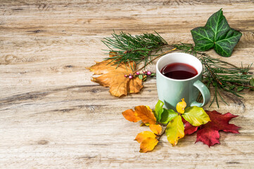 autumn leaves, berries, tea in a mug on a wooden background