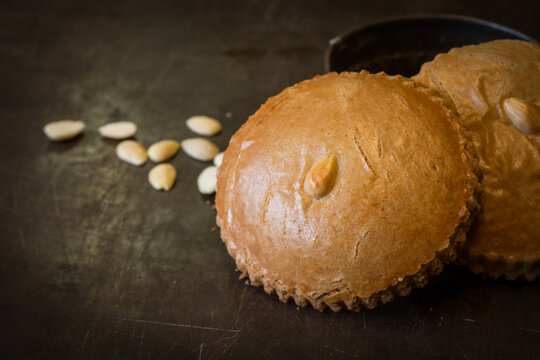 Round traditional  dutch cookie called "gevulde koek" on a metal surface with almonds in the background.