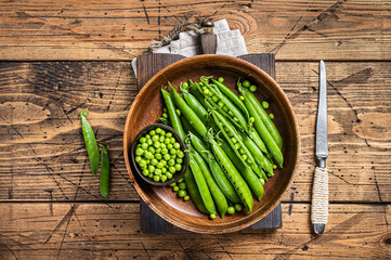 Unpeeled young green pea pods in a wooden plate. wooden background. Top view