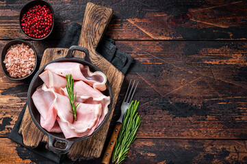 Prosciutto ham sliced in a pan. Dark wooden background. Top view. Copy space - obrazy, fototapety, plakaty