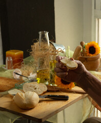Manos de abuelo cortando pan para comer con aceite de oliva delante de una ventana 