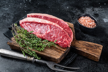 Uncooked Raw rump steak or top sirloin cap beef meat steaks on wooden board. Black background. Top...
