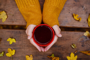 cup of hot tea in female hands holding it on wooden autumn