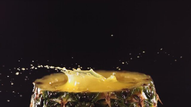 Pineapple pieces falling on the surface of half pineapple in slow motion.