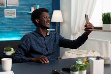 Relaxed handsome student talking selfie using front camera of smartphone during leisure posting on...