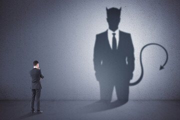 Fototapeta premium Attractive thoughtful young european man with devil shadow standing in empty concrete interior. Disguise, demon and career concept.