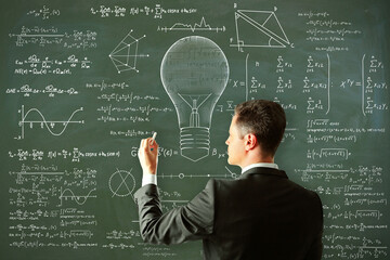 Attractive young european man drawing abstract lamp sketch with mathematical formulas on chalkboard/blackboard wall background. Intelligence, idea, solution, science and innovation concept.