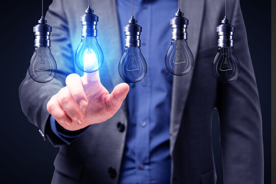 Close up of businessman hand pointing at abstract glowing row of light bulbs on dark background. Idea, solution and innovation concept.