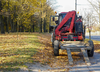 Fototapeta na wymiar Photo of a small red tractor with a crane on the street on the road in the city among the trees