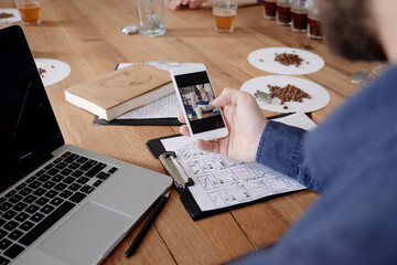 Hand with smart phone screen against wooden table with laptop